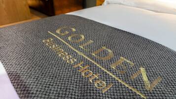 A bed with a textured gray bedspread and the text "GOLDEN BUSINESS HOTEL" embroidered in gold.