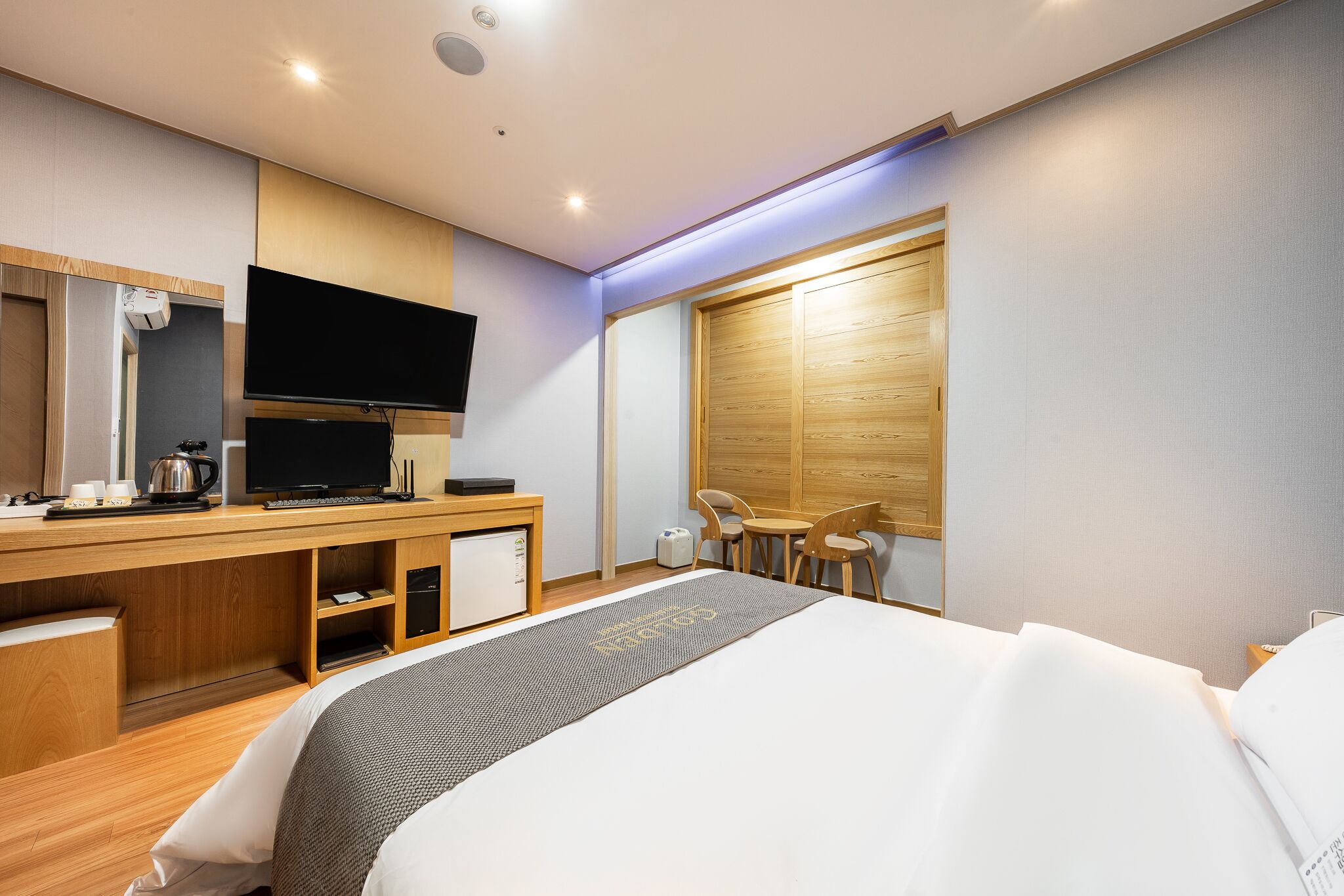 A modern hotel room with a large bed, a desk with a flat-screen TV, a coffee maker, and a small refrigerator.