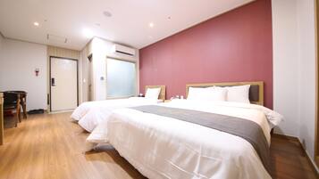 Quarto de hotel com duas camas, piso de madeira, parede com detalhes em vermelho e uma mesa de trabalho com cadeira.