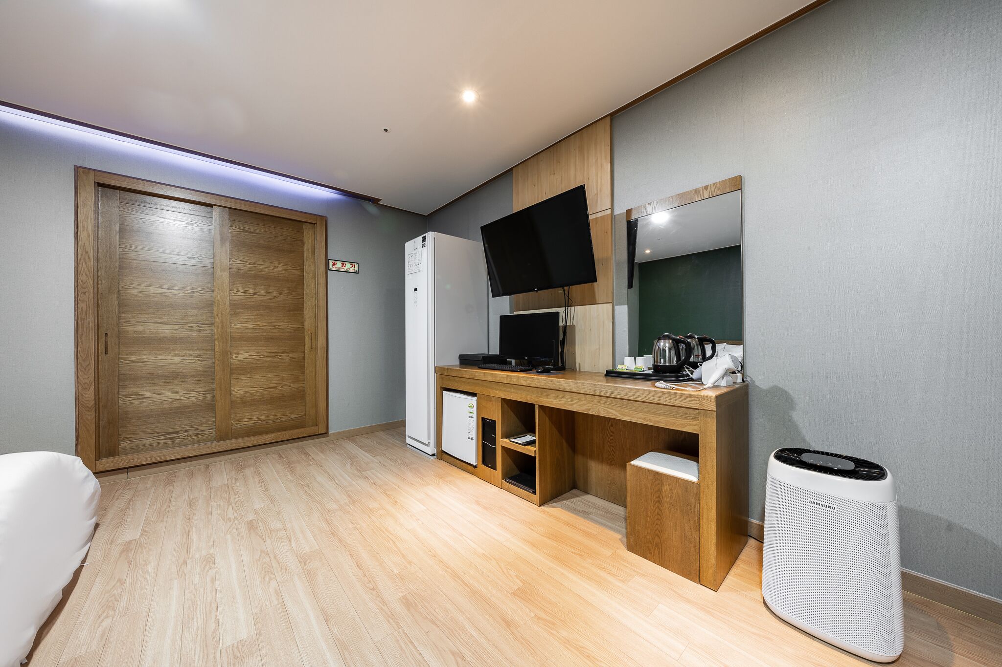 A compact room with a wooden desk, a flat-screen TV, a small refrigerator, and a white heater.