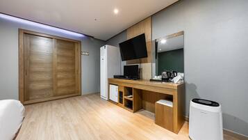 A compact room with a wooden desk, a flat-screen TV, a small refrigerator, and a white heater.