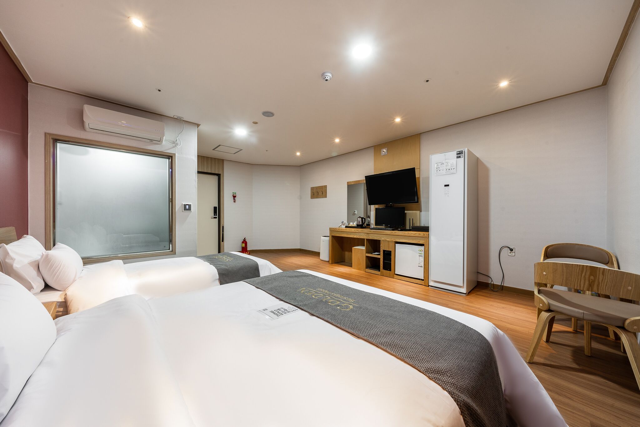 A hotel room with two beds, a TV, a desk, and a chair.