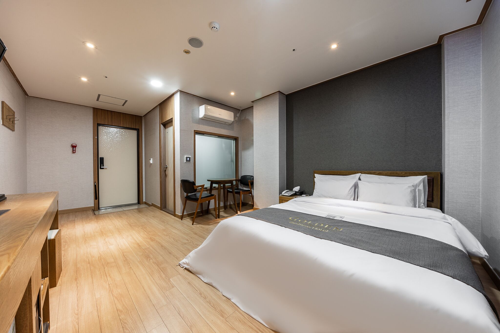 A hotel room with a large bed, a desk, a chair, and a small table.