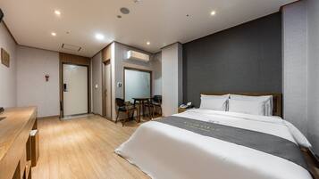 A hotel room with a large bed, a desk, a chair, and a small table.