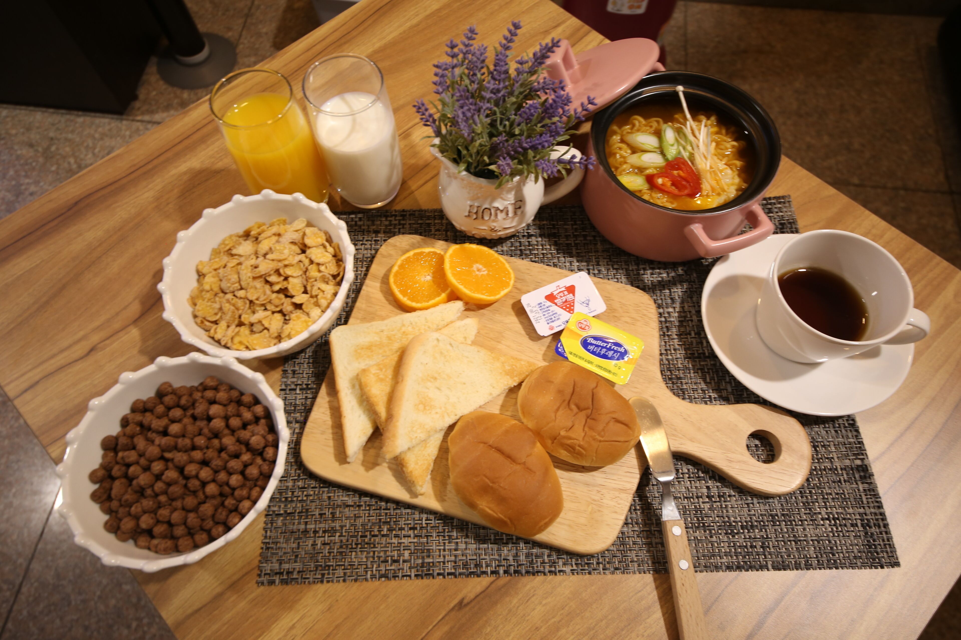 Bandeja de desayuno con cereal, tostadas, rodajas de naranja y una olla de sopa.