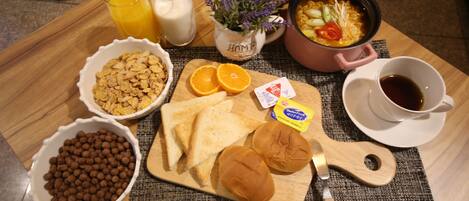 Bandeja de desayuno con cereal, tostadas, rodajas de naranja y una olla de sopa.