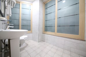 Un baño con un lavabo blanco, inodoro y ventanas con vidrio esmerilado.
