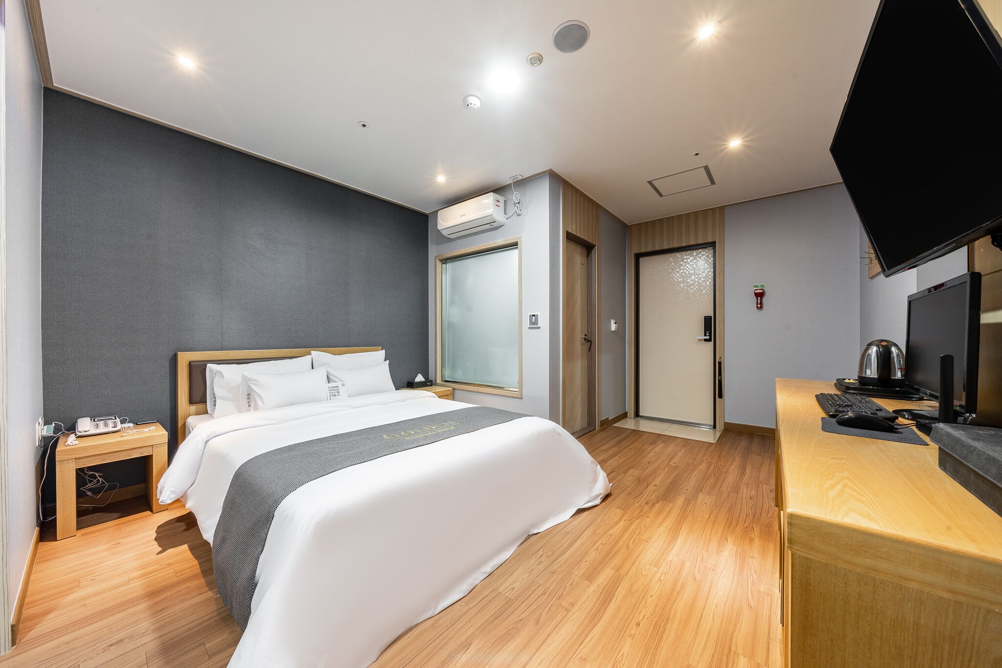 Una habitación de hotel con cama, mesita de noche, televisor y escritorio con computadora.