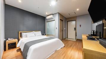 Una habitación de hotel con cama, mesita de noche, televisor y escritorio con computadora.