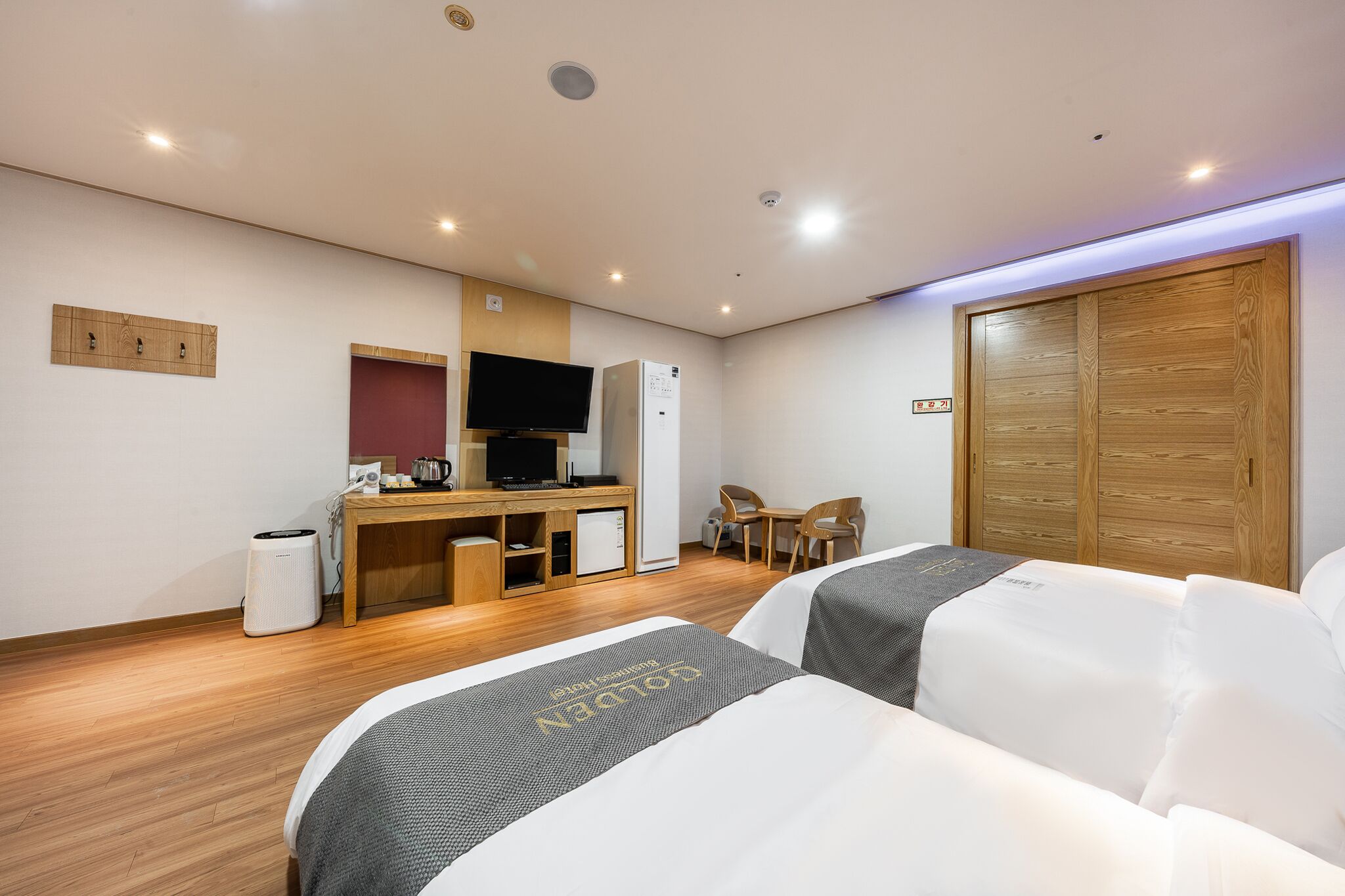 A hotel room with two beds, a desk with a computer, a television, and a wardrobe.