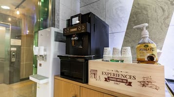 Een koffieapparaat, een fles handdesinfectiemiddel en een houten doos met de tekst 'EXPERIENCES I SHARED WITH YOU 1867' in een hotelomgeving.