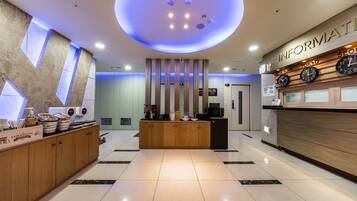 A modern hotel lobby with a reception desk, a clock displaying time in New York, Tokyo, and Seoul, and a large circular light fixture on the ceiling.
