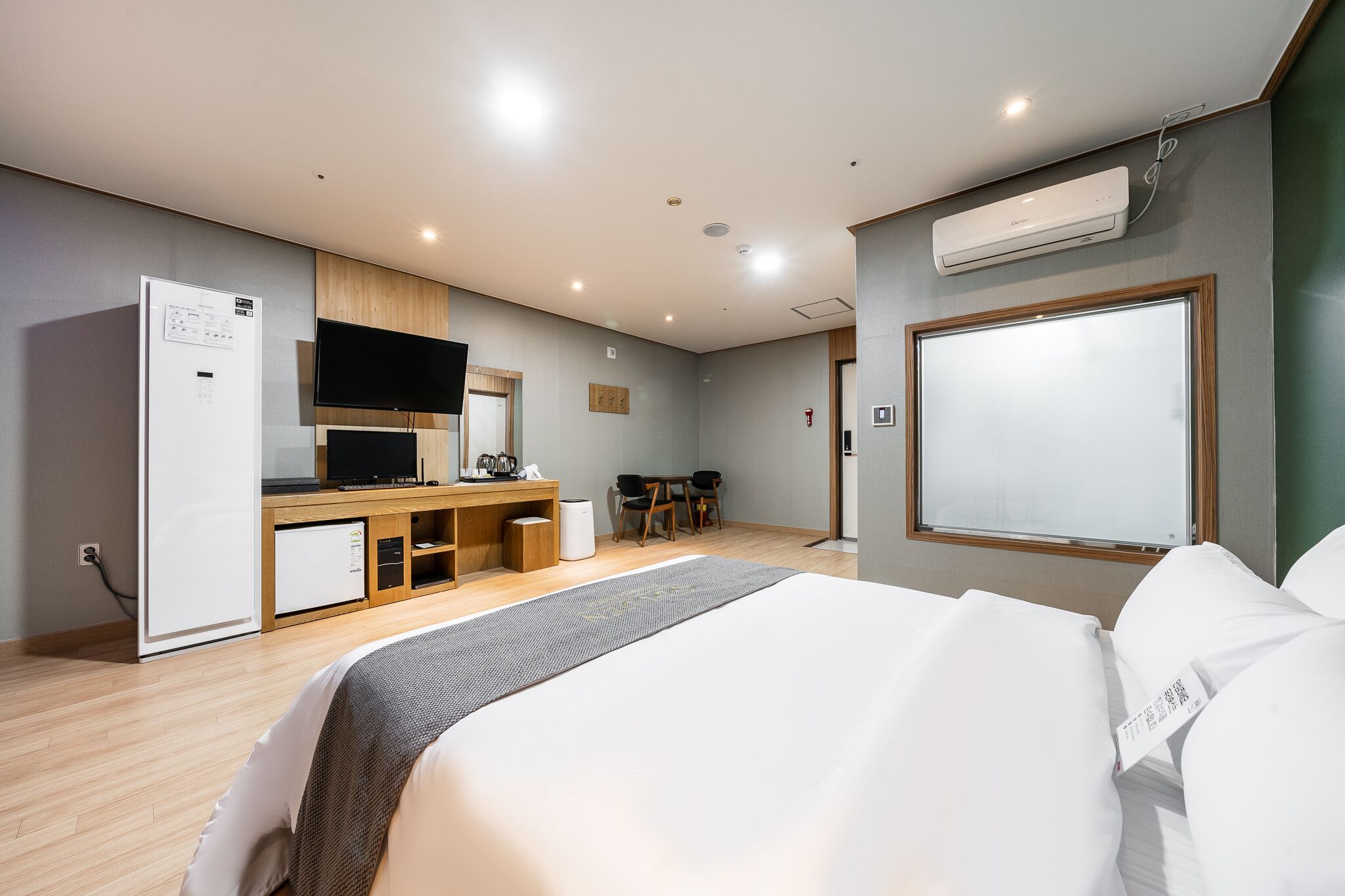 A modern hotel room with a bed, a desk, a television, and an air conditioning unit.