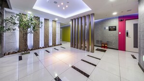 A modern lobby with a clean, tiled floor, a large artificial tree, and a bright ceiling with recessed lighting. - Golden Business Hotel (Seosan)