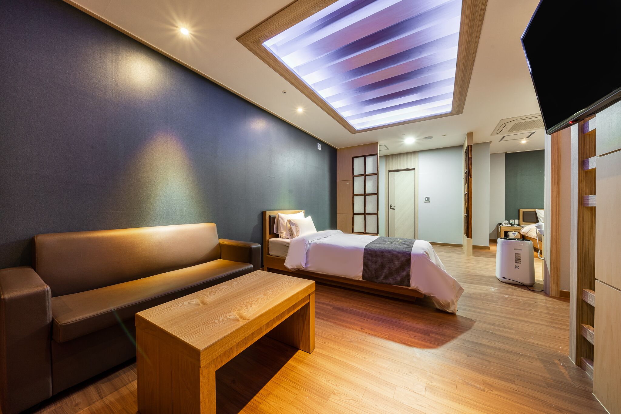 A modern hotel room with a sofa, a bed, a wooden table, and a ceiling skylight.