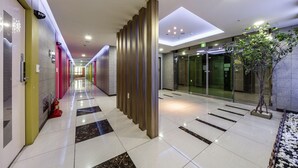 A modern hotel lobby with a check-in counter, a reception desk, and a glass elevator. - Golden Business Hotel (Seosan)