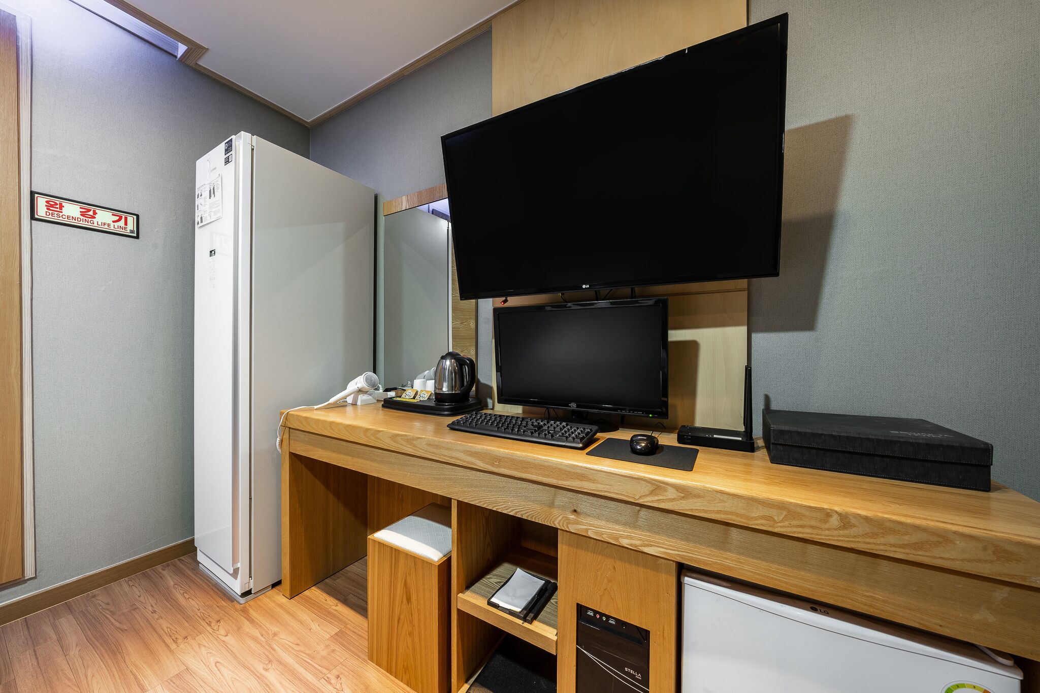 Habitación de hotel compacta con escritorio de madera, televisor de pantalla plana, refrigerador pequeño y lavavajillas integrado.