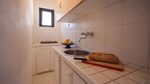 A kitchen with white cabinets, a gas stove, a sink, and a loaf of bread on a cutting board. - Residence La Valdana - 3 room apartment with swimming pool, tennis and parking 1km from the beach (Capoliveri)