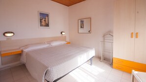 A bedroom with a bed, bedside table, wardrobe, and wall-mounted light fixtures. - Residence La Valdana - 3 room apartment with swimming pool, tennis and parking 1km from the beach (Capoliveri)