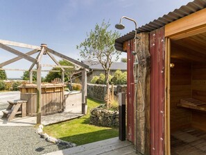 Un sauna extérieur en bois, doté d’une douche, d’une terrasse en bois et d’un mur en pierre.