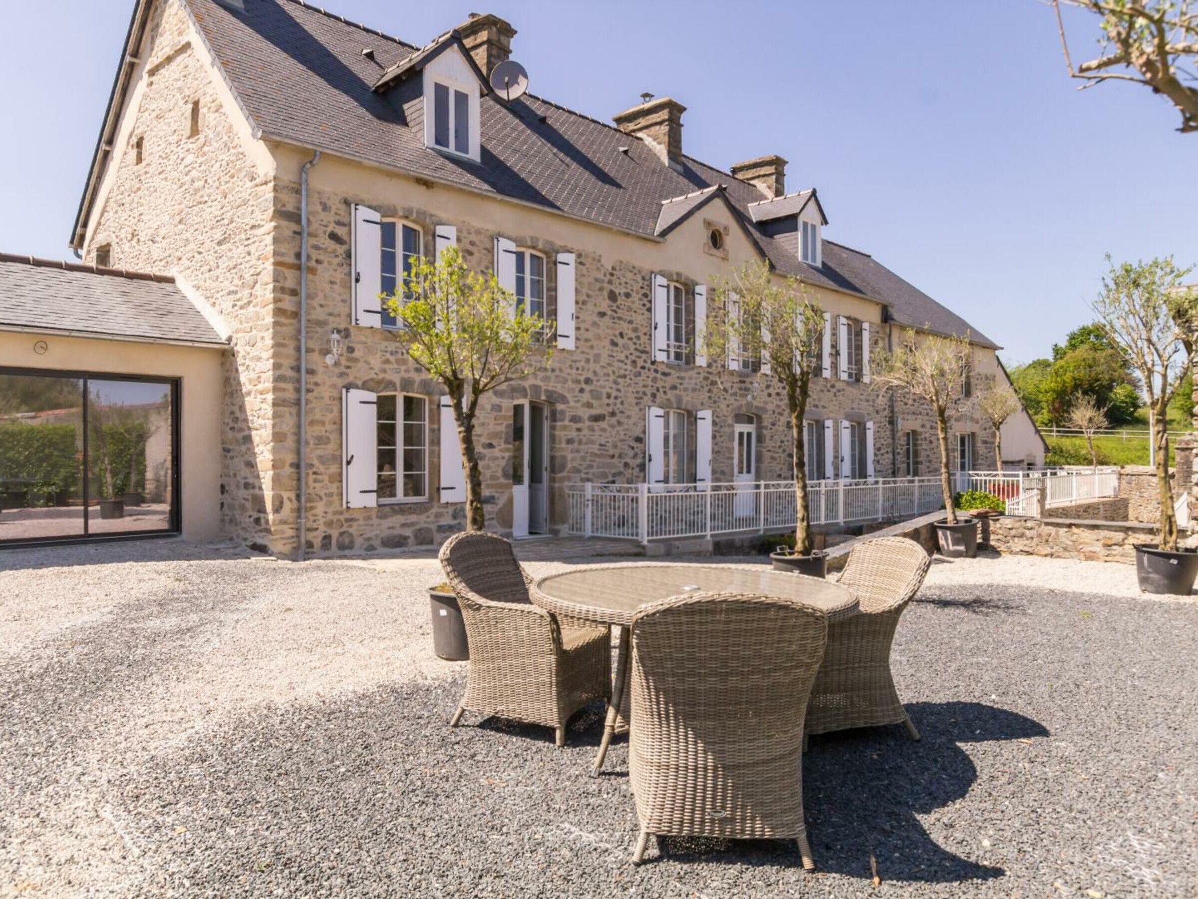 A stone building with a gravel patio, wicker furniture, and a white fence.