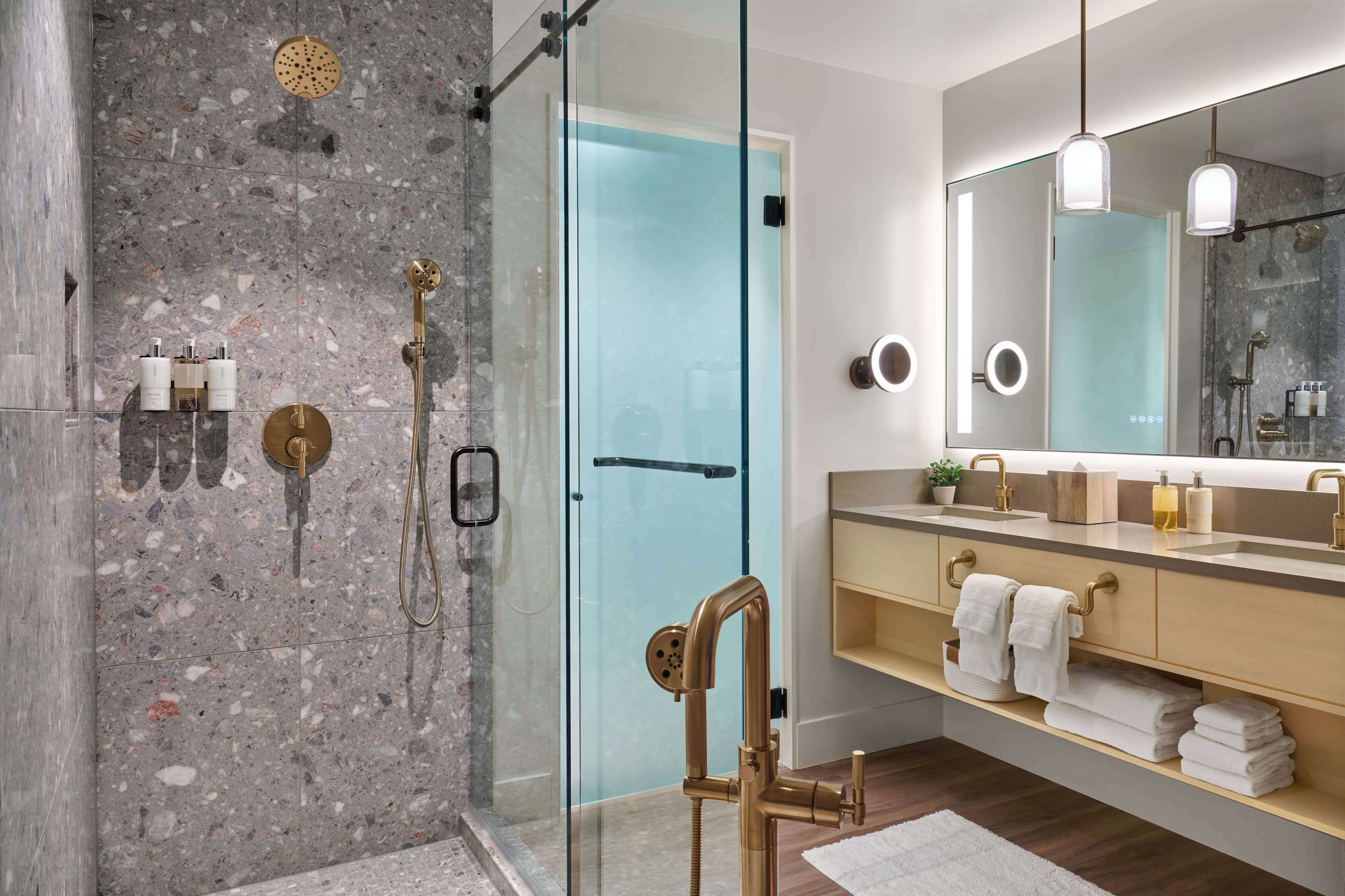A modern bathroom with a glass shower enclosure, a large mirror, and a wooden vanity with towels.