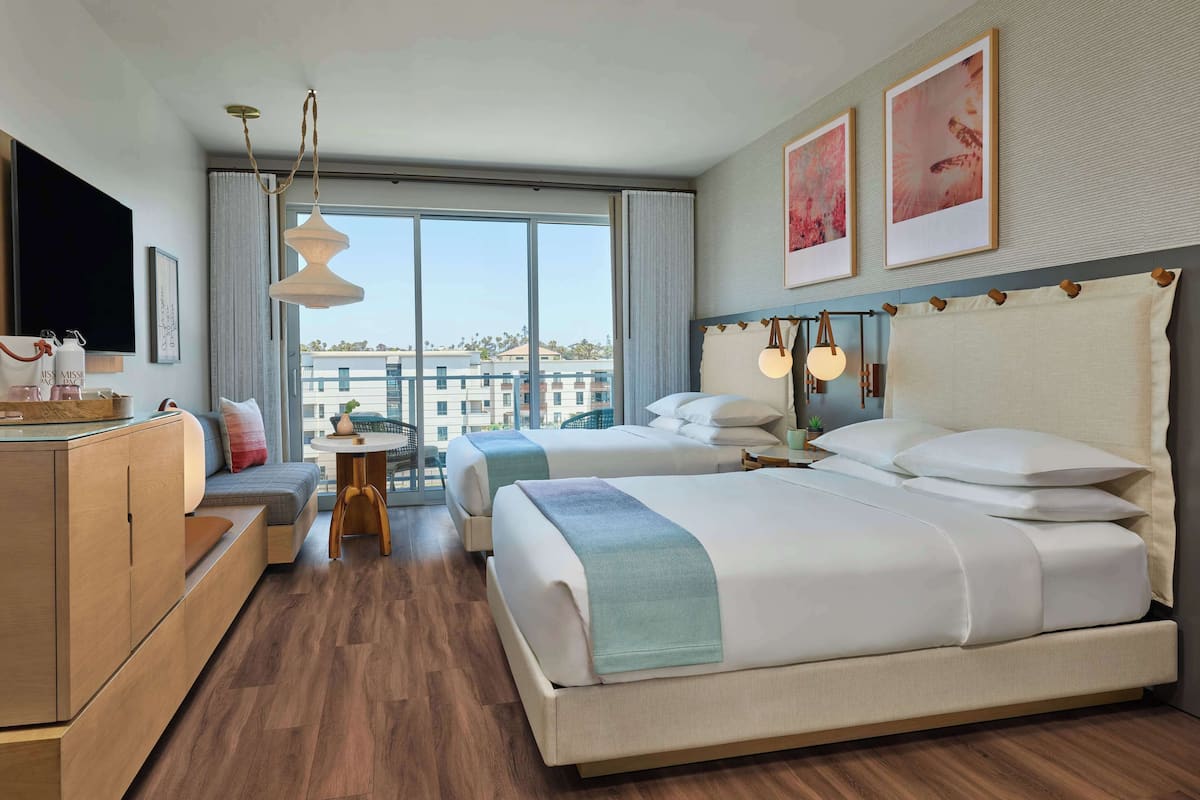 Habitación de hotel con dos camas, un sofá, un televisor y un ventanal con vistas a la ciudad.