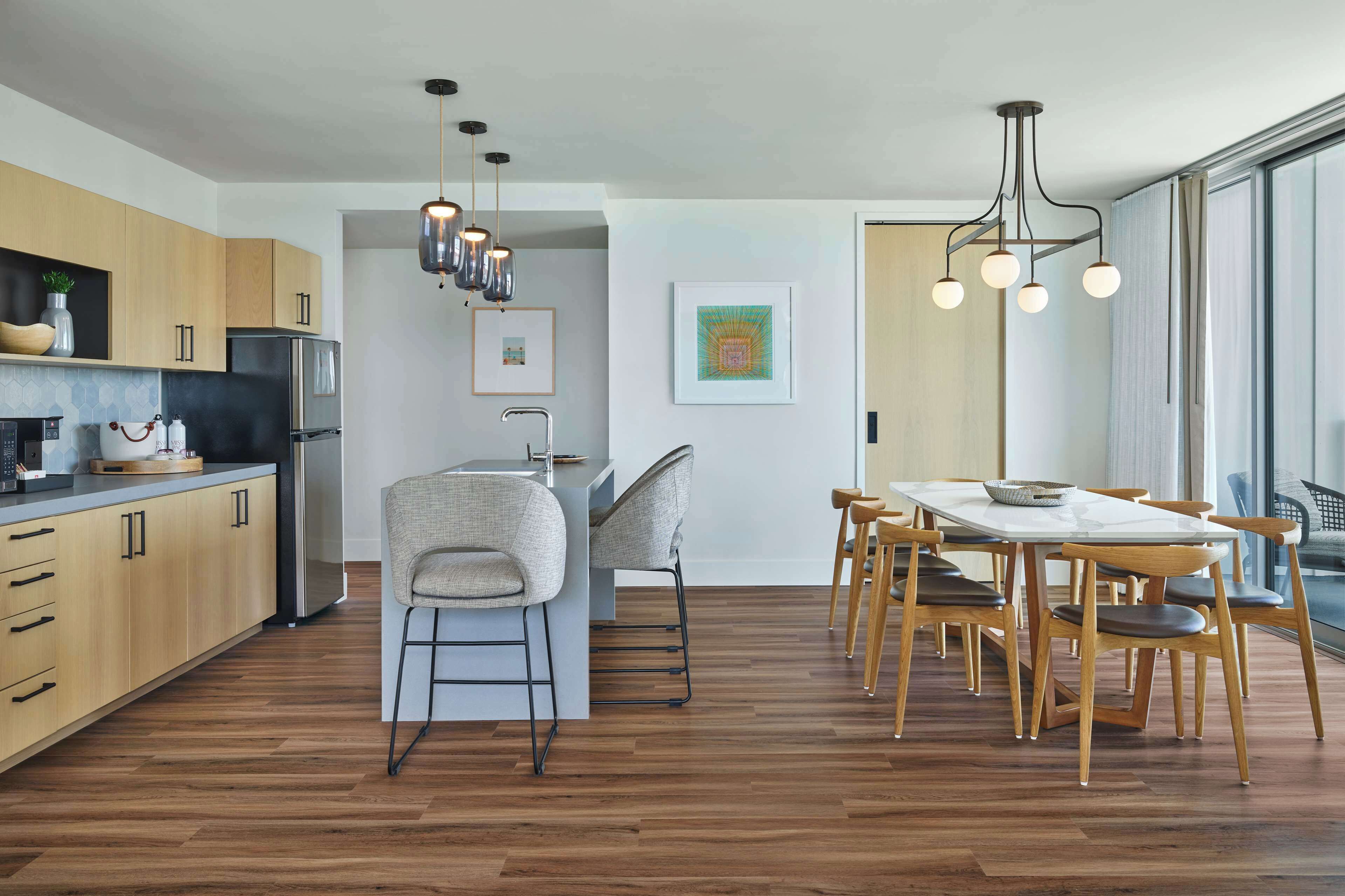 Una cocina moderna con armarios de madera, una isla central y una zona de comedor con mesa y sillas de madera.