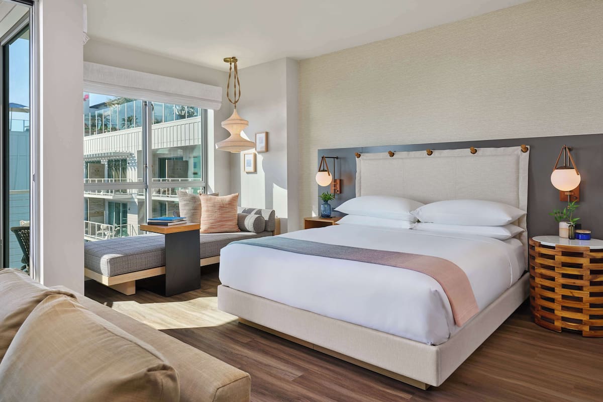 Una habitación de hotel moderna con una cama grande, un área de descanso con vistas y un balcón.