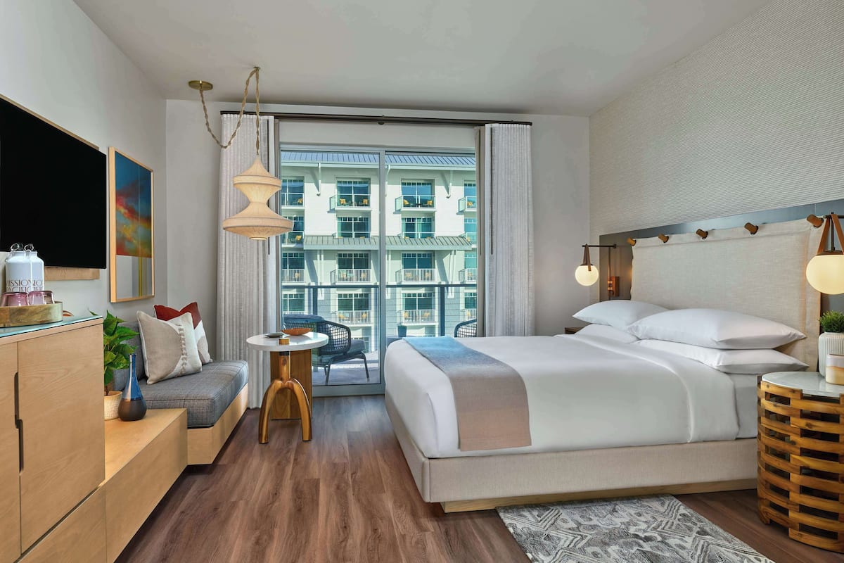 Una habitación de hotel moderna con una cama grande, un sofá, una mesita y un televisor.