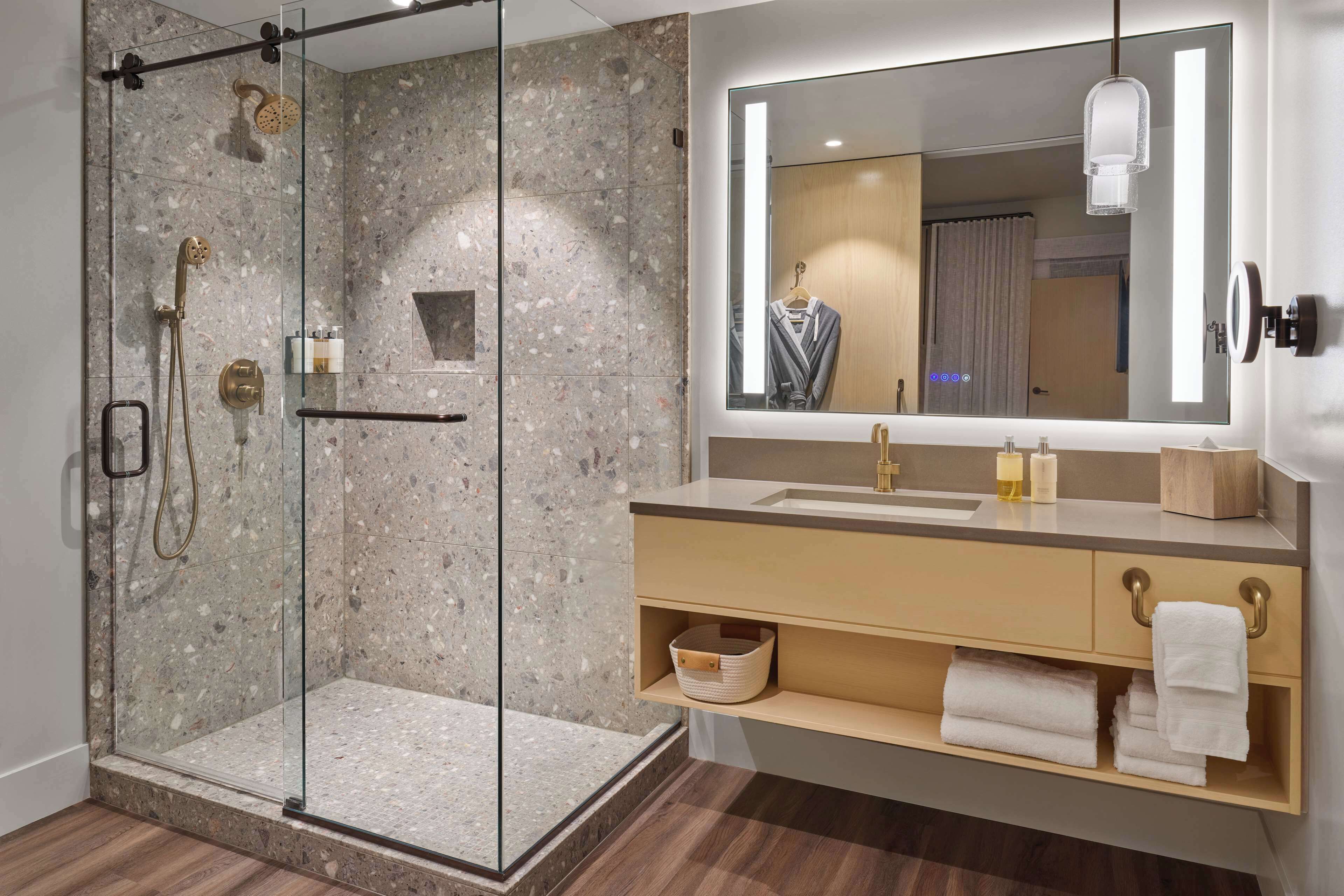 A modern bathroom with a glass-enclosed shower, a large mirror, and a vanity with a sink and towel storage.