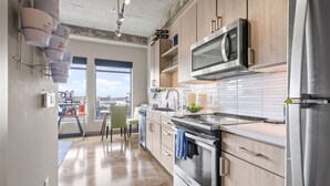 A modern kitchen with wooden cabinets, stainless steel appliances, and a large window offering a city view.