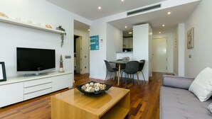 Un salon moderne avec un téléviseur à écran plat, une table basse en bois, un canapé gris et un coin repas comprenant une table et des chaises.