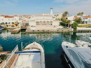 Un puerto deportivo con varias embarcaciones amarradas, un edificio blanco destacado con arcos y un faro al fondo.