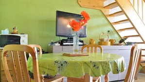 A dining area with a green table, wooden chairs, a television, and a vase with flowers.