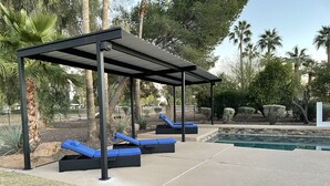 Un'area esterna coperta con poltrone relax e una piscina.