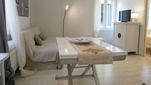 A modern, minimalist bedroom with a bed, bedside table, and a television on a cabinet. - CASA ADRIA (Alghero)