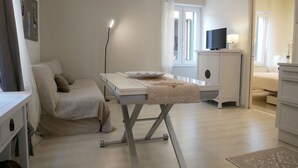A bedroom with a bed, bedside table, TV, and a desk with a lamp. - CASA ADRIA (Alghero)
