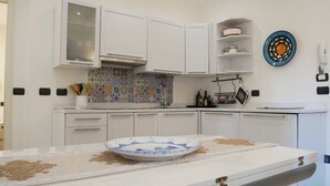 A modern kitchen with white cabinets, a tiled backsplash, and a decorative plate on the counter. - CASA ADRIA (Alghero)