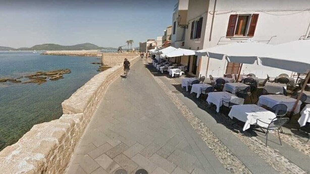A seaside walkway with outdoor seating, a stone wall, and a view of the sea. - CASA ADRIA (Alghero)