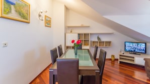 A dining area with a glass-top table, six chairs, and a vase with flowers. There is a television on a stand to the right. - Apartment Sun & Sky (Dubrovnik)