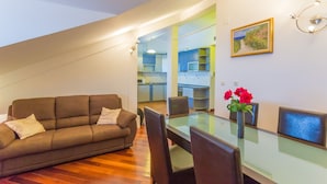 A modern living room with a glass dining table, brown sofa, and a kitchen visible through an open door. - Apartment Sun & Sky (Dubrovnik)