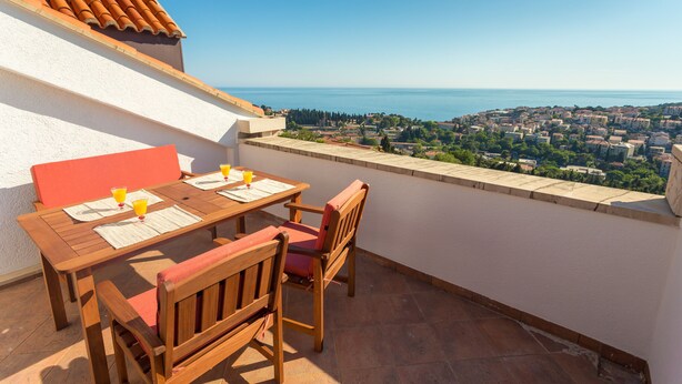 A terrace with a wooden table and chairs, overlooking a coastal town. - Apartment Sun & Sky (Dubrovnik)