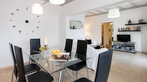A modern dining area with a glass table, black chairs, and a wall clock. There is a bookshelf and a television in the background. - Villa Cesar (Corfu)