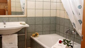 A bathroom with a sink, mirror, and bathtub. There are towels and a rose on the bathtub. - Di Palai Hotel (Zakynthos)