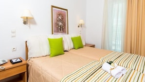 A hotel room with a bed, two pillows, a bedside table with a lamp, a framed picture on the wall, and a window with curtains. - Di Palai Hotel (Zakynthos)