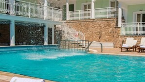 A swimming pool with clear blue water, a stone wall, and a white railing. There are lounge chairs and towels on the poolside. - Di Palai Hotel (Zakynthos)
