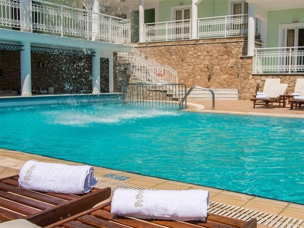 A swimming pool with clear blue water, a stone wall, and a white railing. There are lounge chairs and towels on the poolside. - Di Palai Hotel (Zakynthos)