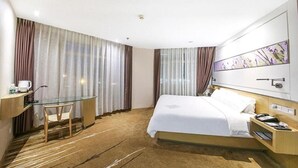Una habitación de hotel con cama, escritorio y silla, un separador de vidrio y un ventanal con cortinas.