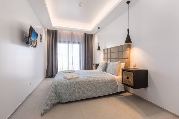 Une chambre à coucher moderne avec un grand lit, un téléviseur fixé au mur, une table de chevet et un luminaire au plafond.